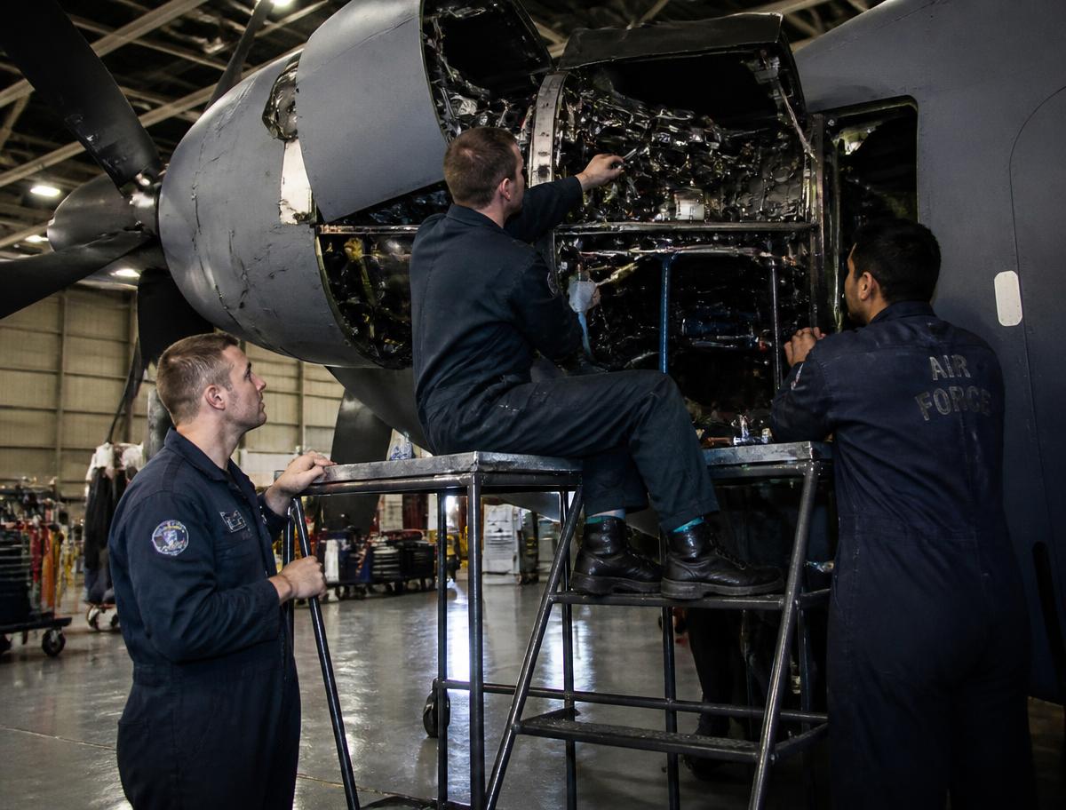 Aircraft maintenance technicians working on a military transport aircraft engine in a hangar